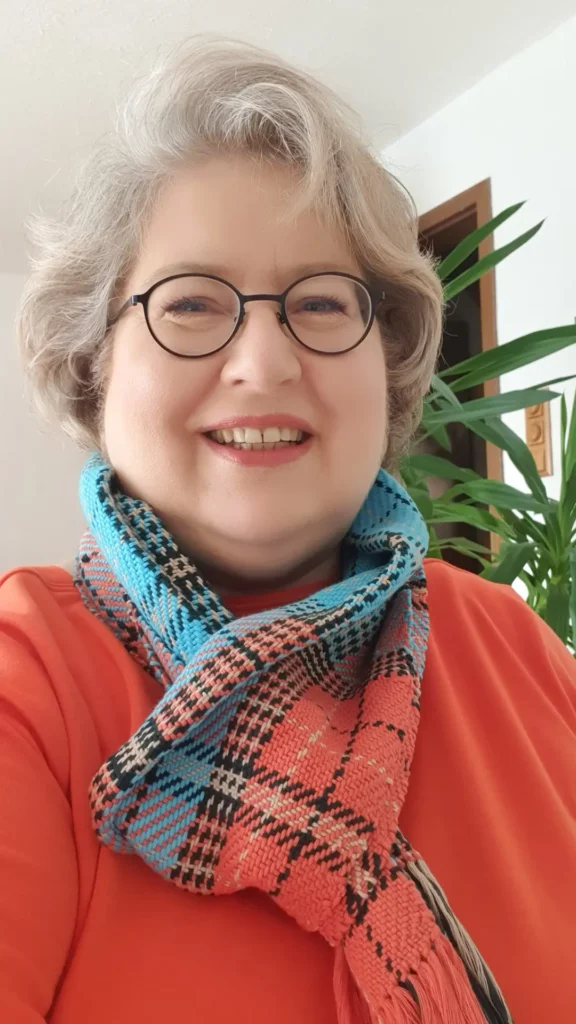 Sandra Dirks trägt den fertig gewebten Karo-Schal in Türkis, Koralle und Orange locker um den Hals zum orangefarbenen Shirt