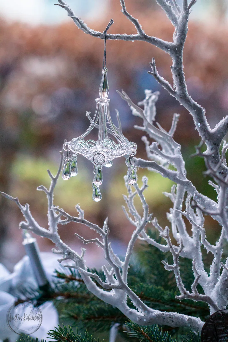 Kleiner Kronleuchter aus klarem Acryl mit funkelnden Glastropfen an einem weiß beschneiten Dekozweig