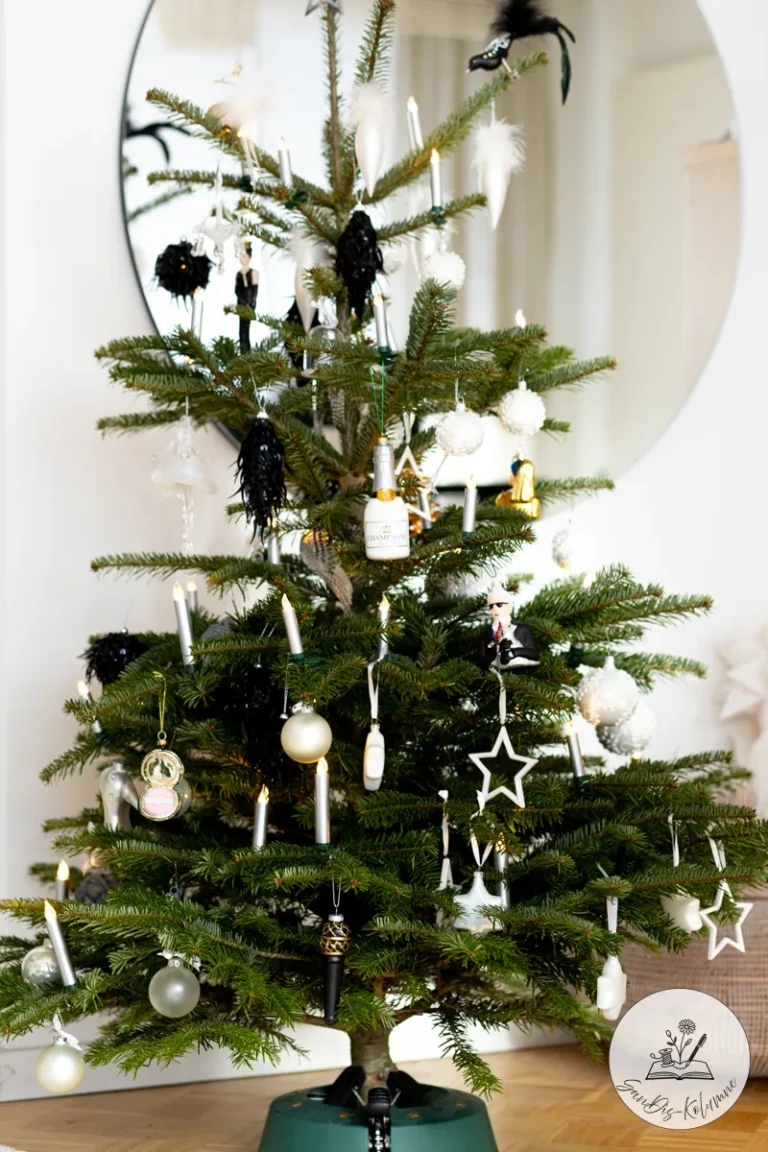 Weihnachtsbaum mit schwarz-weißem Schmuck: kleine Karl-Lagerfeld-Figur, Champagnerflasche und Federn zwischen LED-Kerzen