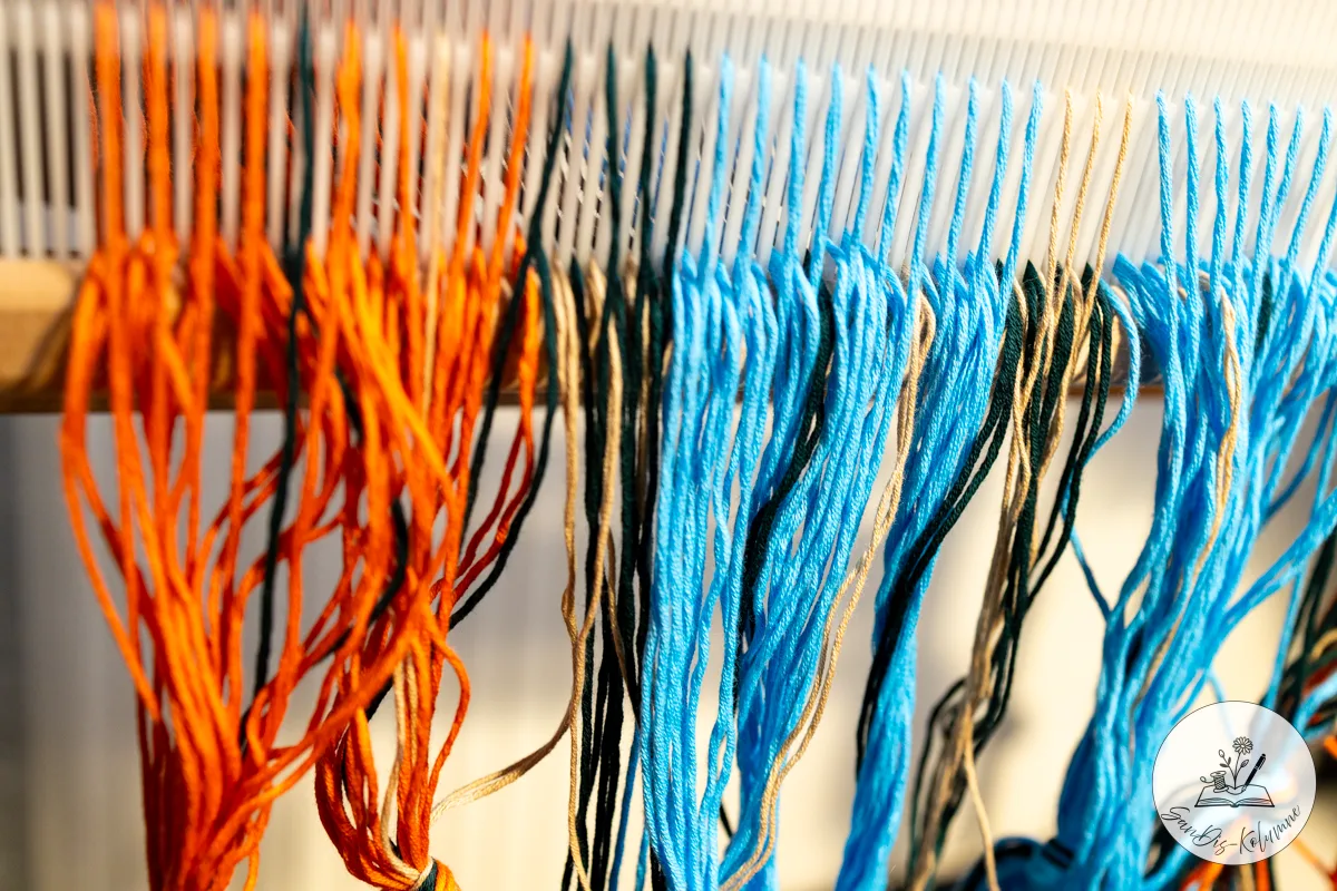 Orange, hellblaue und petrolfarbene Fadenbündel hängen dicht an dicht durch die Zähne des Gatterkamms