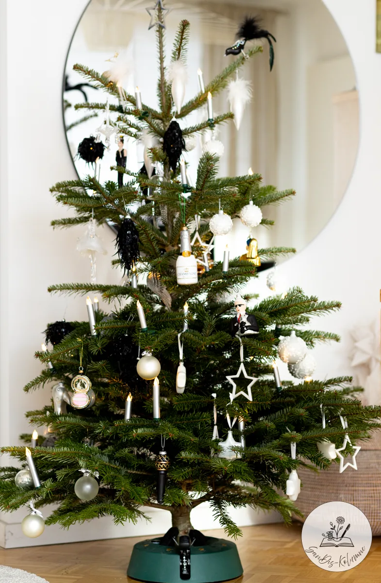 Der ganze schwarz-weiß geschmückte Weihnachtsbaum im grünen Ständer auf Parkett, dahinter der runde Wandspiegel