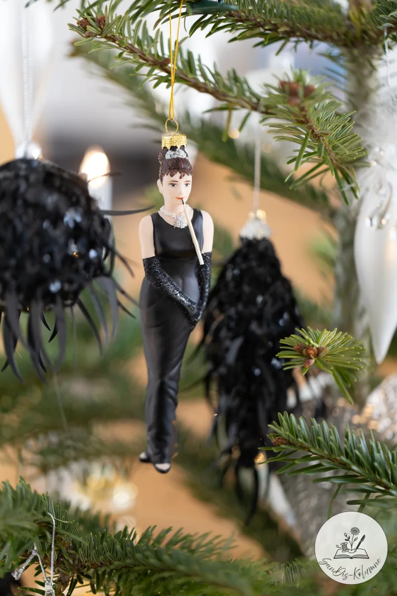 Die Audrey-Hepburn-Figur mit langen Glitzerhandschuhen frontal zwischen zwei schwarzen Pailletten-Anhängern im Tannengrün