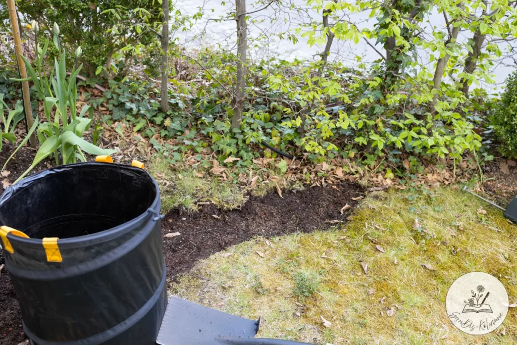 Blick am schwarzen Gartensack vorbei auf die frisch abgestochene Rasenkante der neuen Beetform
