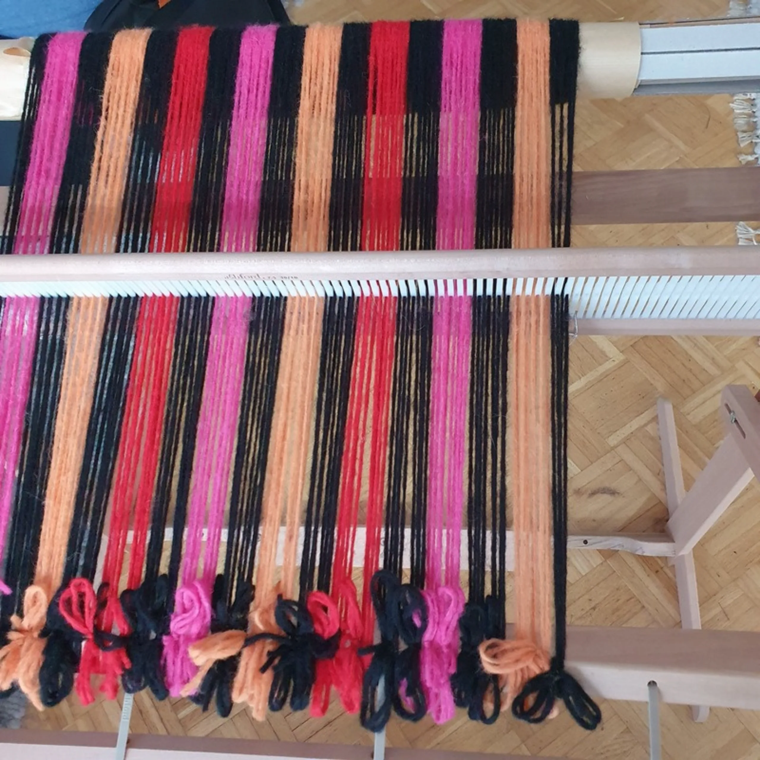 Die aufgespannte Kette des Stern-Schals von der Seite, die Farbblöcke in Pink, Orange, Rot und Schwarz wechseln sich ab