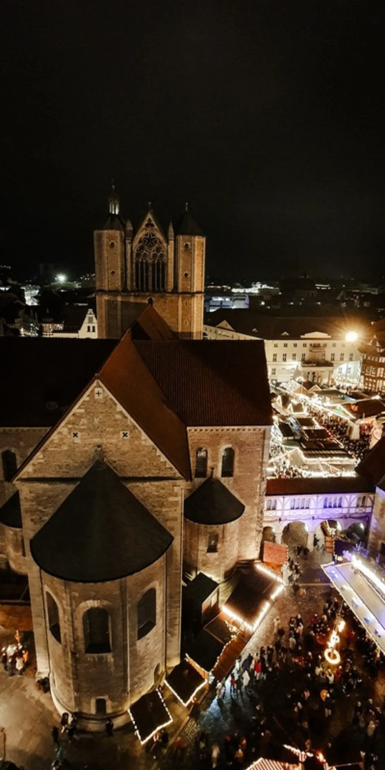 Blick vom Rathausturm auf den Braunschweiger Dom und die leuchtenden Stände des Weihnachtsmarkts auf dem Burgplatz