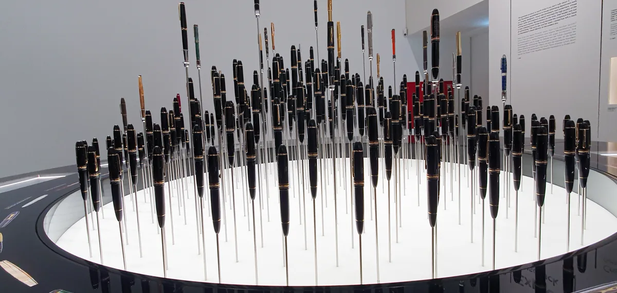 Die kreisförmige Füller-Installation aus der Distanz: zwischen Schwarz-Gold auch Modelle in Grün, Bordeaux und Silber, hinten eine rote Vitrine.