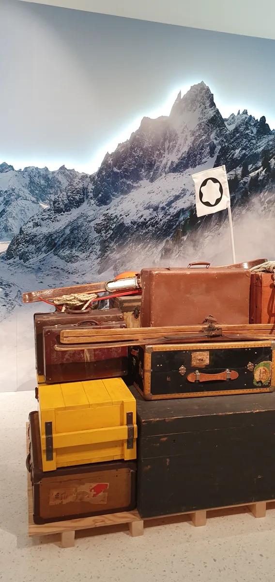 Der Requisiten-Stapel aus Koffern, Truhe und gelber Holzkiste vor dem dramatisch hinterleuchteten Berggipfel, dazwischen die Montblanc-Fahne.