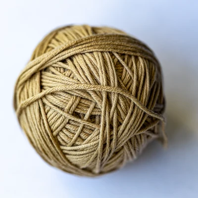 Ein beiges Wollknäuel, selbst gewickelt, von oben auf weißem Grund