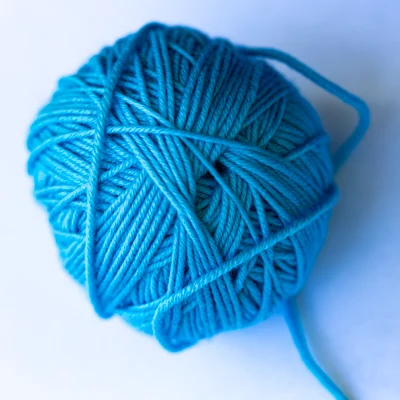 Ein hellblaues Wollknäuel, selbst gewickelt, von oben auf weißem Grund