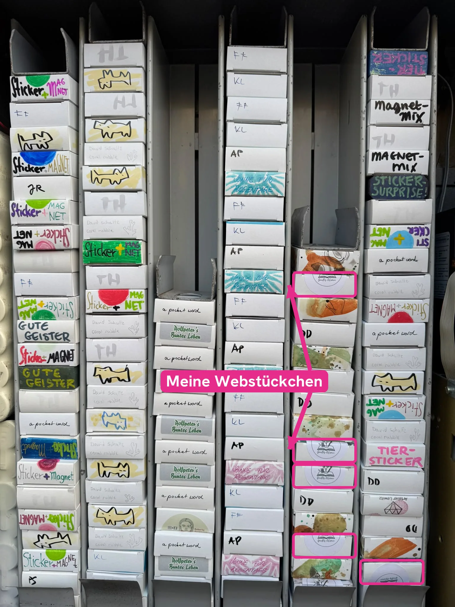 Blick in den geöffneten Kunstautomaten mit sechs Schachtelreihen, die Schachteln mit dem runden SanDis-Kolumne-Stempel sind pink umrandet und mit Meine Webstückchen beschriftet.
