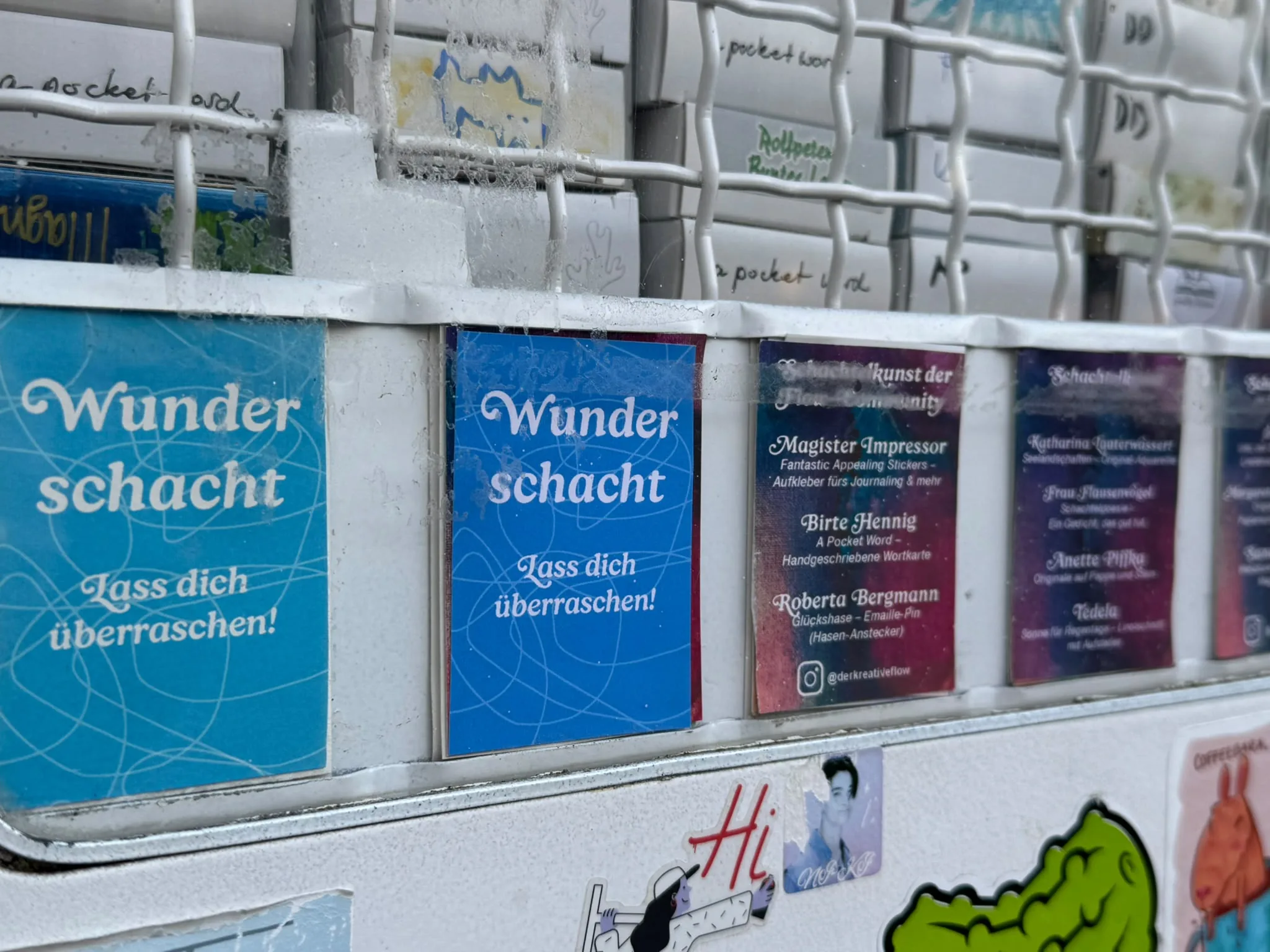 Blaue Karten mit der Aufschrift Wunderschacht, Lass dich überraschen, stecken neben den Künstlerlisten im Ausgabefach des Kunstautomaten.